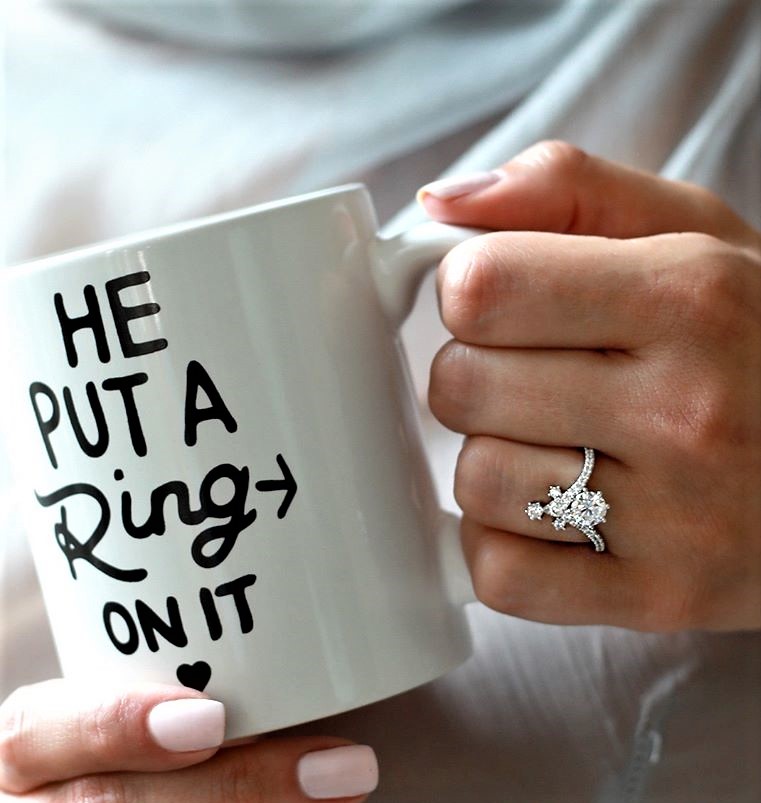 A woman's hand showing off a stunning floral-style diamond engagement ring, holding a celebratory mug, from the bridal collection at Catawba Island Jewelers in Port Clinton, Ohio.